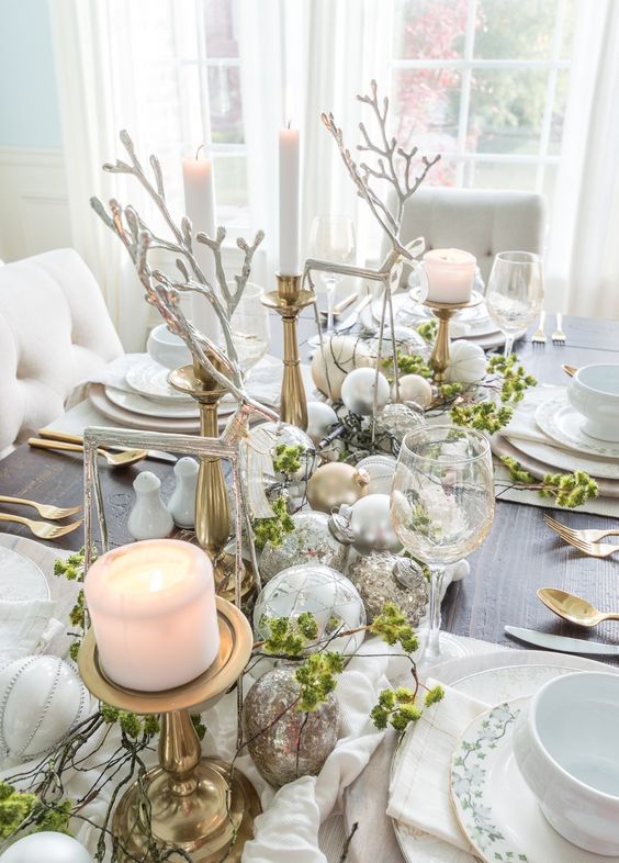 a creative NYE wedding centerpiece of silver and mercury glass ornaments, tall and thin candles, frame deer and pillar candles and greenery