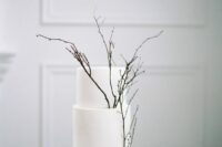 a crispy white minimalist wedding cake decorated with black twigs is a great idea for a minimalist spring wedding