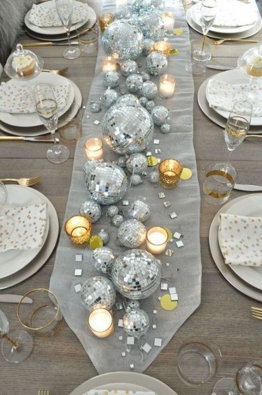 a fabric table runner with silver disco balls, candles and some shiny mirror pieces is a creative centerpiece alternative for a NYE wedding
