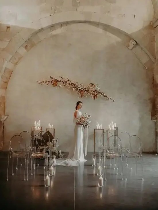 a fantastic minimalist wedding space with a blooming branch arrangement and candles for the altar plus ghost chairs lined up with candles