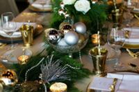 a festive table runner with evergreens, candles, beads and Christmas ornaments in a metallic bowl