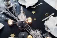 a glam NYE wedding tablescape with a black table, gold and glitter stars, candles, sivler branches and star napkin rings
