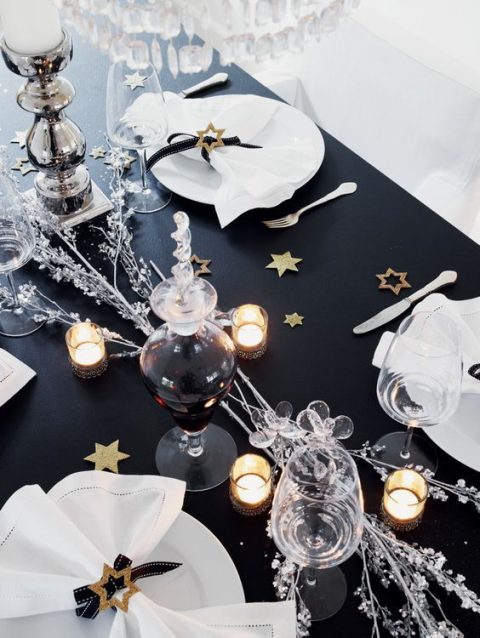 a glam NYE wedding tablescape with a black table, gold and glitter stars, candles, sivler branches and star napkin rings