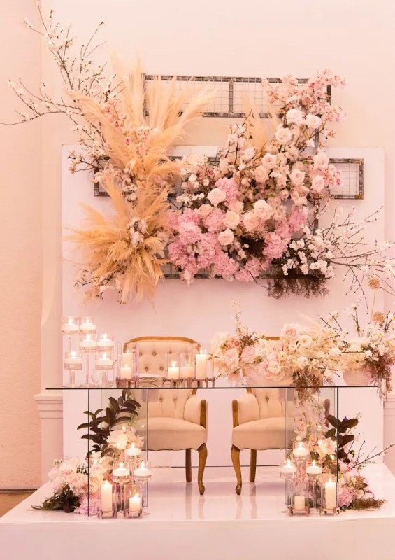 a glam and refined wedding sweetheart table with blooms at the base and a jaw-dropping floral installation behind, no foam used