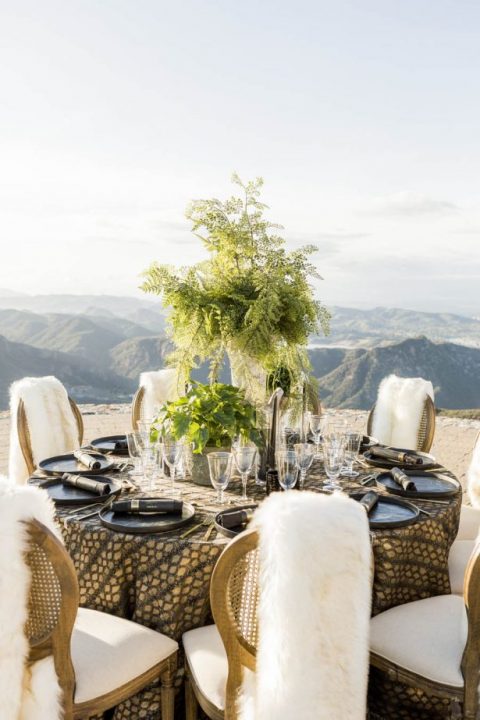a glam black and gold tablescape with chargers and black napkins, greenery in pots and vases
