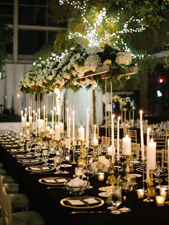 a gorgeous glam NYE wedding tablescape with pillar and thin and tall candles, a tall centerpiece with white hydrangeas and greenery