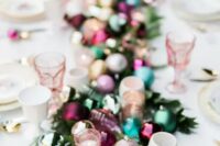 a gorgeous table runner made of candle holders, greenery and colorful Christmas ornaments