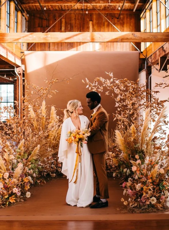 a gorgeous warm-colored wedding altar made with pampas grass, dried leaves and bold warm-colored blooms without any foam