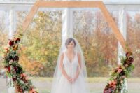 a hexagon wedding arch with greenery and dark and bold flowers and candle lanterns hanging for a fall wedding
