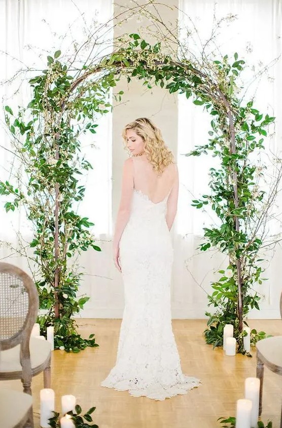 a lovely spring wedding arch decorated with greenery and some blooming branches and accented with candles