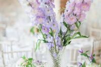 a lovely tall wedding centerpiece of white, lilac and blush delphinium and greenery in smaller vases around is cool