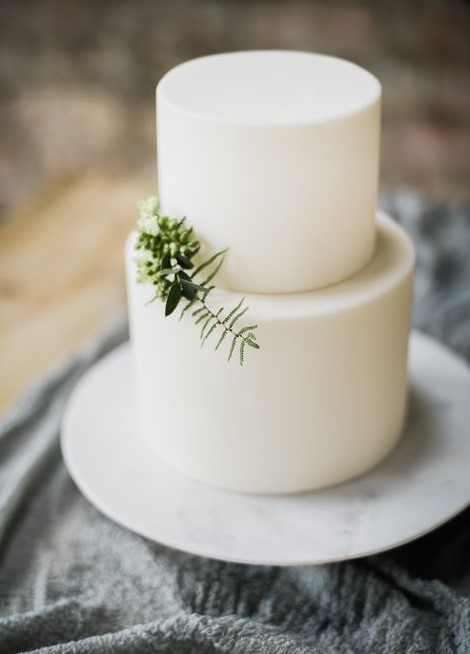 a minimalist plain white wedding cake topped with only a touch of greenery is a beautiful idea with no fuss