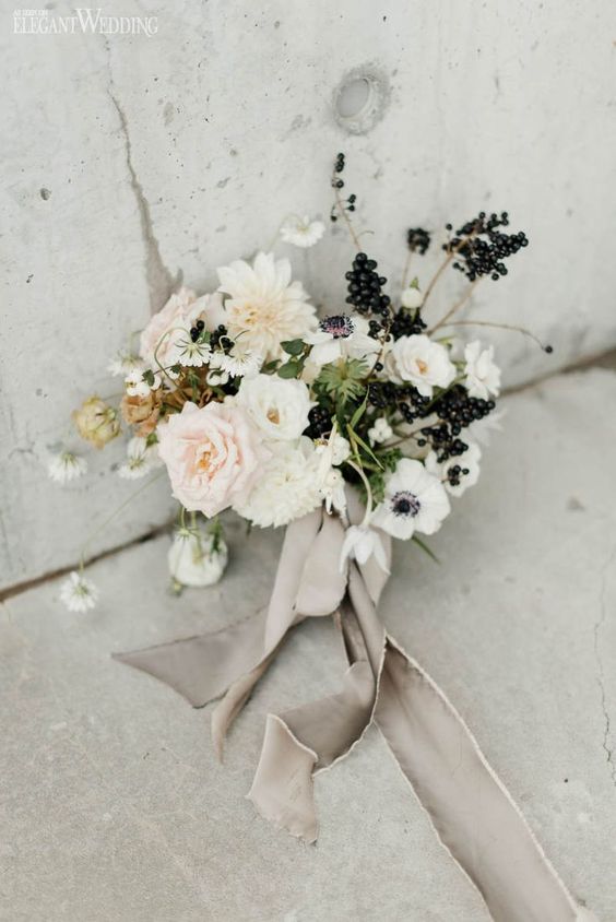a modern black and white wedding bouquet that includes anemones, dahlias, berries and twigs and some neutral ribbons