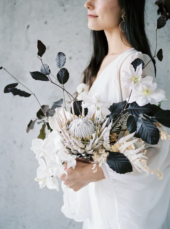 a modern black and white wedding bouquet with white blooms, black foliage and dried grasses plus a king protea is unique