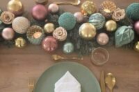 a muted color NYE wedding tablescape with pink, green and gold ornamnets, evergreens and candles, green plates and gold cutlery