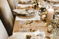 a neutral and metallic wedding tablescape with shiny candles, gold rim plates, glasses and metallic cutlery