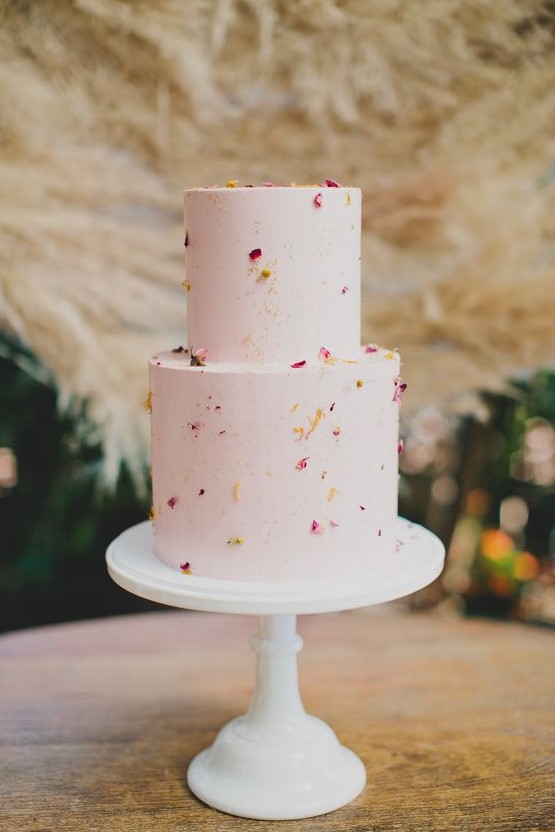 a playful two-tier wedding cake in light pink, with gold speckles and flower petals on it is a perfect idea for spring