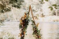 a pretty boho fall triangle wedding arch done with greenery, rust, blush and pink blooms, dried grasses and leaves