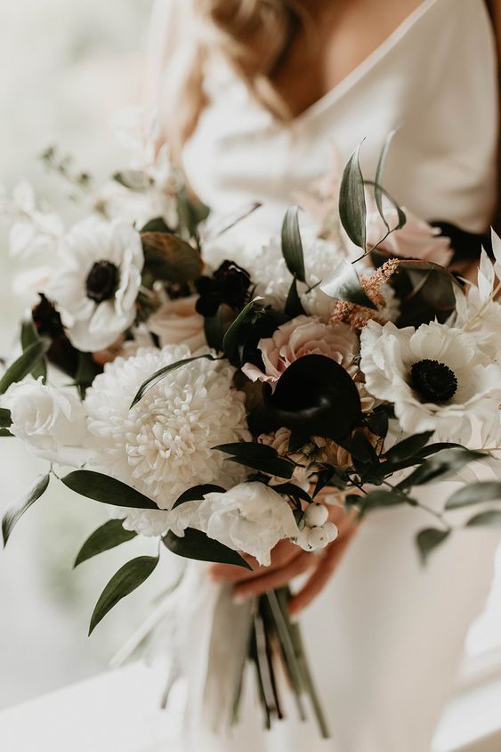 a pretty dimensional wedding bouquet of white roses, anemones, black callas and some blush roses and leaves is wow