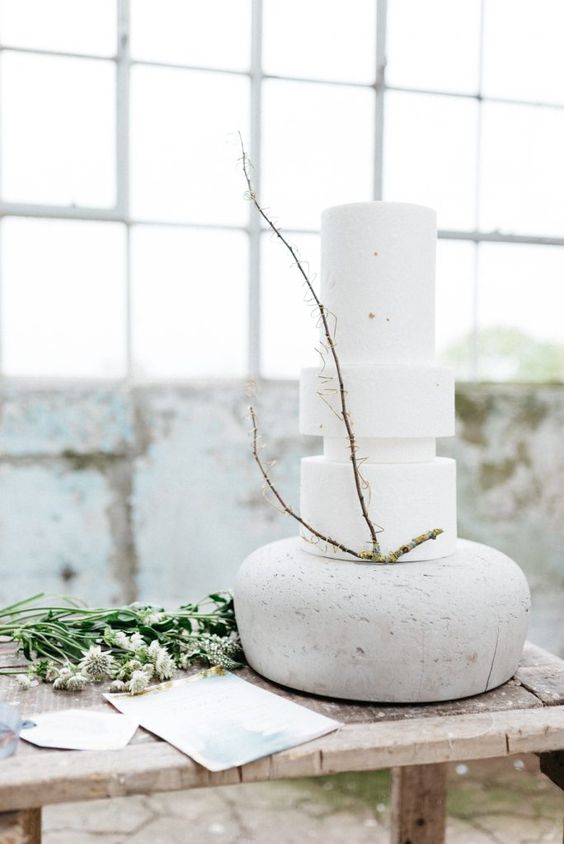 a pure white minimalist wedding cake of mismatching round tiers and with a bit of green branches for a spring minimalist wedding