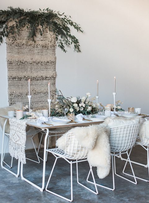 a refined white winter wedding tablescape with a macrame runner, white candles and candleholders and a lush white centerpiece