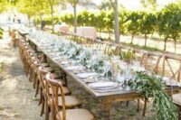 a rustic wedding reception with a lush greenery table runner and vintage dark-stained furniture, neutral porcelain and clear glasses