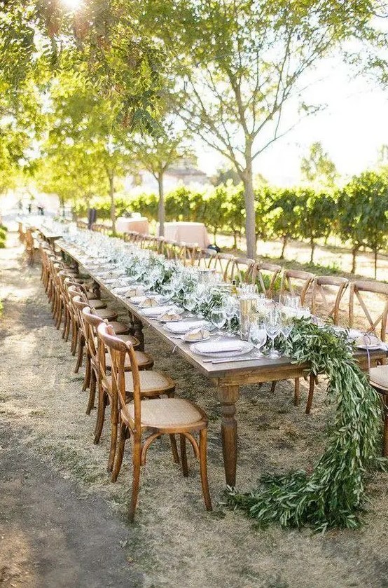 a rustic wedding reception with a lush greenery table runner and vintage dark-stained furniture, neutral porcelain and clear glasses