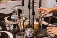 a shiny NYE wedding centerpiece composed of disco balls, tall and thin black candles in black candleholders and usual gold candleholders