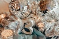 a shiny NYE wedding centerpiece of silver sequin fabric, silver disco balls and candles plus a silver table number