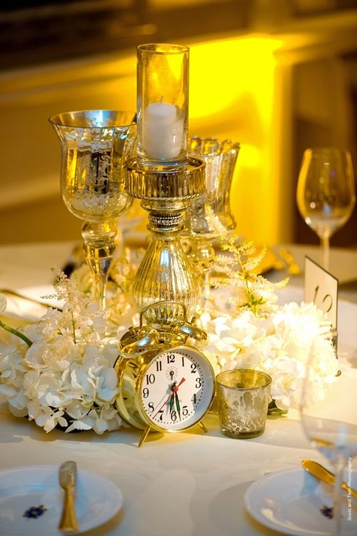 a shiny NYE wedding centerpiece of white hydrangeas, mercury glass candleholders and a clock is a cool and easy to repeat idea