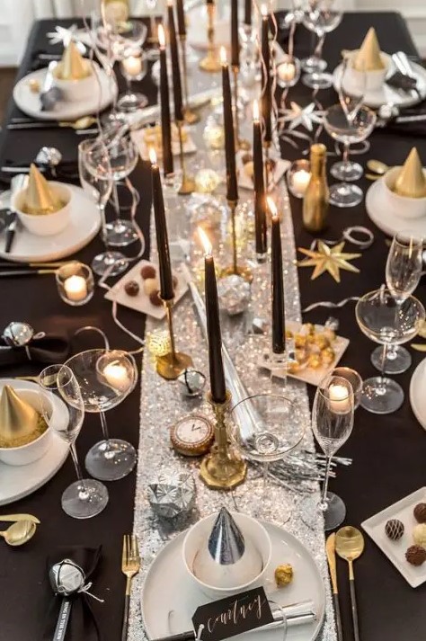 a shiny NYE wedding table with a silver runner, gold stars, silver bells, black candles, clocks and gold cones