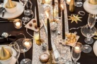 a shiny NYE wedding table with a silver runner, gold stars, silver bells, black candles, clocks and gold cones