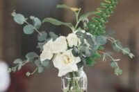 a simple and stylish wedding centerpiece with white garden roses, fern and eucalyptus and a couple of candles on each side