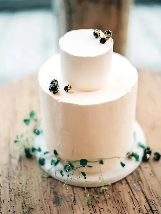 a simple frosted cake decorated with gilded berries and greenery is a beautiful idea for a minimalist fall wedding
