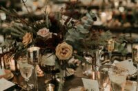 a sophisticated NYE wedding table setting with a black tablecloth, bold and neutral blooms and greenery, candles and gold-rimmed glasses