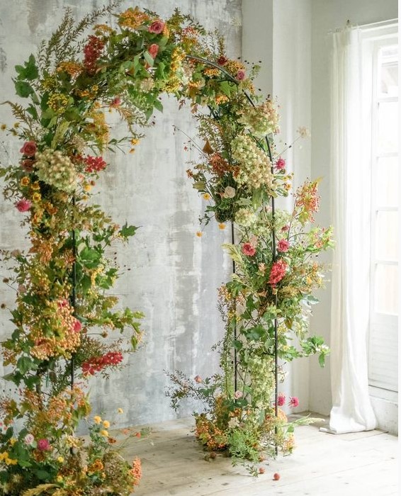 a sophisticated fall wedding arch done with greenery and foliage and bright yellow, orange and pink blooms is amazing