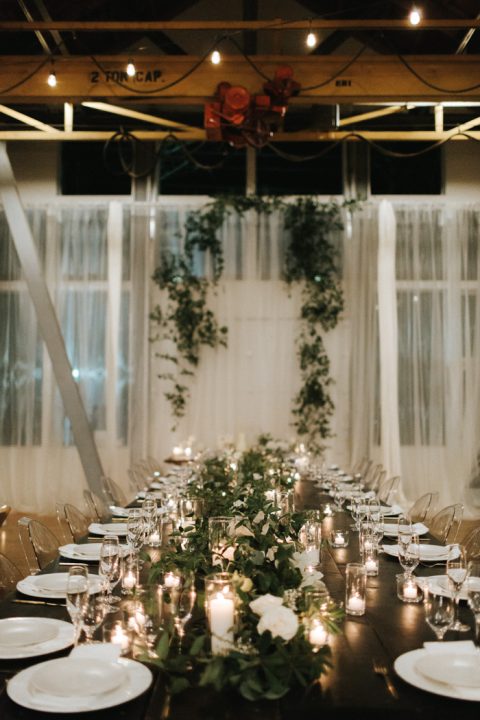 a stylish and simple tablescape with a black table, a greenery and white bloom runner, candles and white porcelain