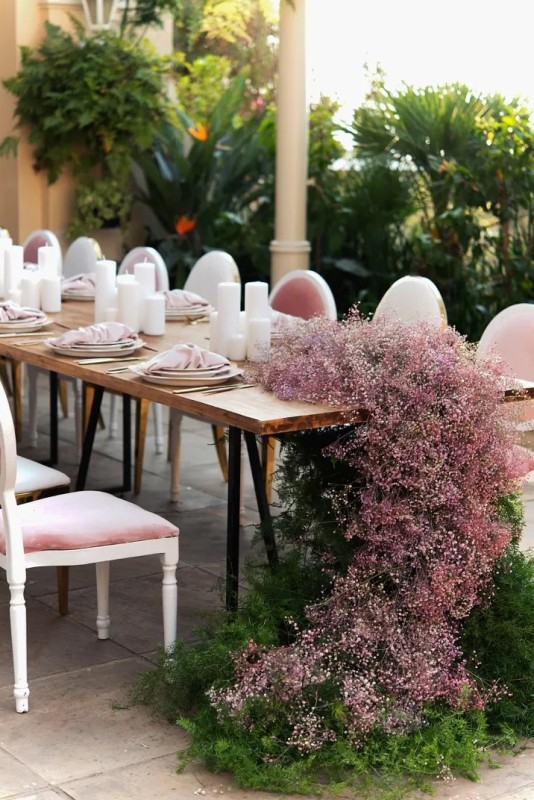 a stylish modern wedding reception table decorated with pink baby's breath and greenery with no foam and pink napkins and pillar candles