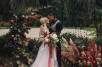 a unique foam free wedding altar made of greenery, pink roses, neutral and red spary painted pampas grass is amazing