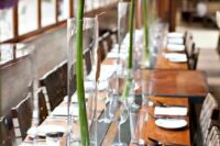 a very laconic modern wedding tablescape with an uncovered table, tall glass vases with allium is a chic and lovely idea