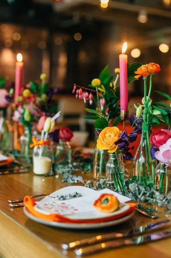 a wedding tablescape accented with super colorful flowers, pink candles and orange napkins looks vibrant