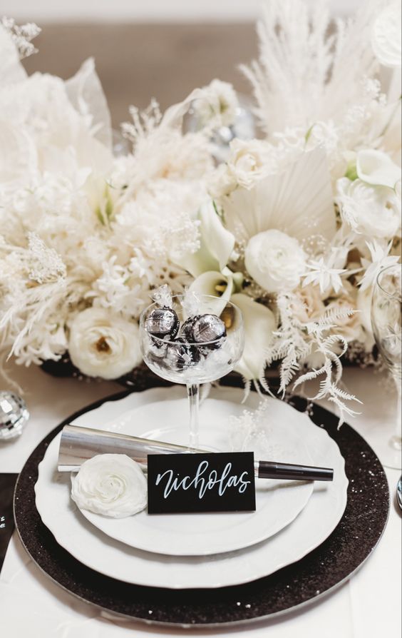 a white floral wedding centerpiece with fronds, grasses and blooms and a glass with tiny ornaments for a NYE wedding