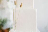 a white minimalist wedding cake of a square shape, decorated with just three twigs of dried grasses
