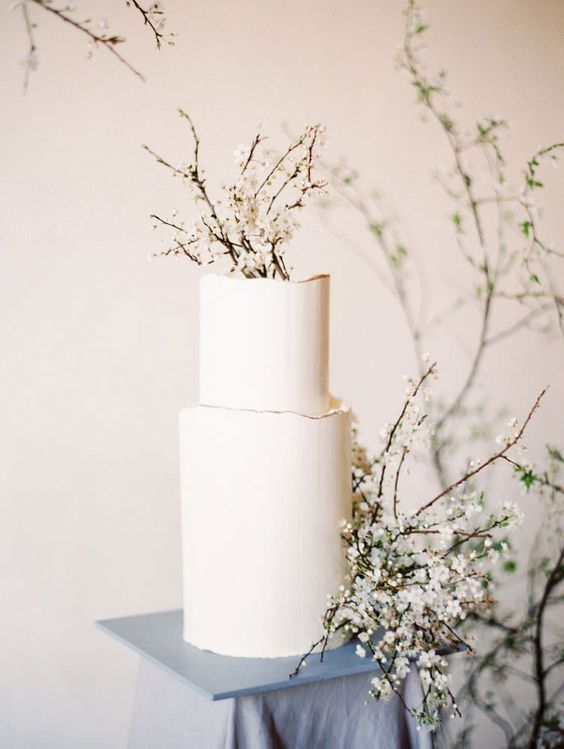 a white wedding cake with a raw edge and some blooming branches is a gorgeous idea for a minimalist spring wedding