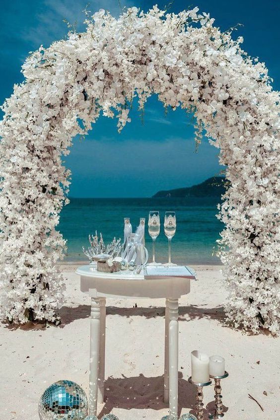a breathtaking white wedding arch completely covered with blooms plus an ocean view are a bold combo for a ceremony