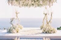 03 a breathtaking wedding ceremony space with a sea view, an acrylic arch with lush white florals, pillar candles lining up the aisle