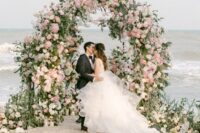 04 a beautiful and lush curved wedding arch covered with greenery, neutral and blush blooms and with a matching wedding aisle plus a sea view