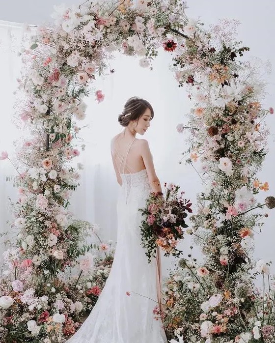 a fabulous and delicate spring wedding arch with white, blush and light pink blooms and greenery balanced with a bit of dark ones