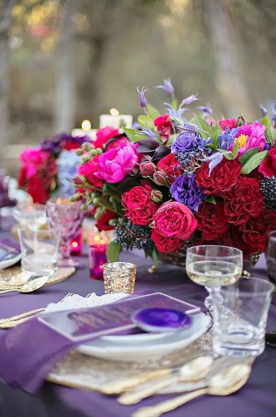 a fab jewel tone wedding centerpiece of red, deep red, hot pink, violet blooms, privet berries and greenery is a chic idea