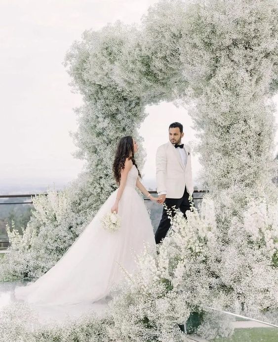 a jaw dropping wedding arch that feels like a cloud as it's fully covered with white baby's breath is amazing